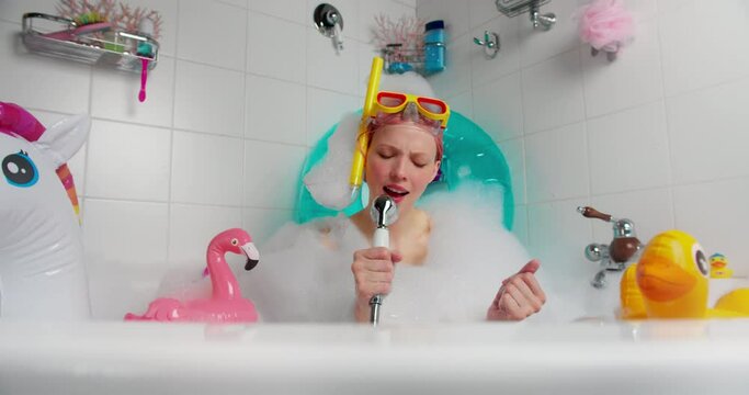 Funny female in a bathing mask sings in the shower with an inflatable duck and a flamingo