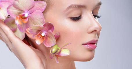 Beautiful woman with Orchid Flowers. Perfect Skin. Professional Makeup. Skincare concept.