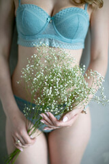 Young girl in lingerie on a background of a gray wall holding flowers.Minimal fashion design concept.