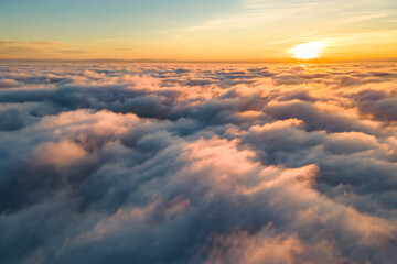 Aerial view of bright yellow sunset over white dense clouds with blue sky overhead. - Powered by Adobe
