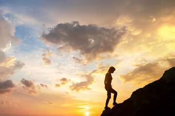 Fototapeta na wymiar Silhouette of a woman hiker climbing up a big stone at sunset in mountains. Female tourist on high rock in evening nature. Tourism, traveling and healthy lifestyle concept.