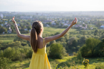 Young woman standing in green field enjoying sunset view in evening nature. Relaxation and meditation concept.