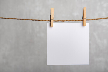One blank square note paper card hanging with wooden clip or clothespin on rope string peg. Copy space