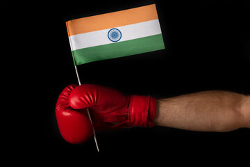 Boxer hand holds flag of India. Boxing glove with the Indian flag. Black background.