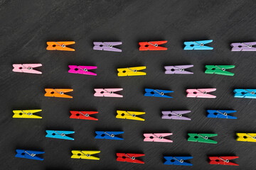 Bright multicolored clothespins lies are in one direction on black background. Diversity