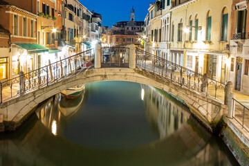 Fototapeta na wymiar Night view of illuminated old architecture, floating boats and light reflections in canals water in Venice, Italy.