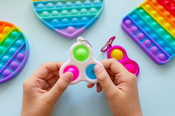 colorful trendy antistress sensory toy fidget push pop it and simple dimple in kid's hands on blue background