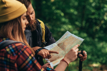 Couple of hikers using trekking poles and map while wearing backpacks