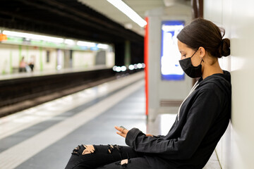 Pretty girl using her mobile phone while waiting for the train in the underground railway. Blurred background and copy space for text.