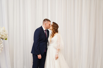 beautiful and happy bride and groom against the background of the white curtain