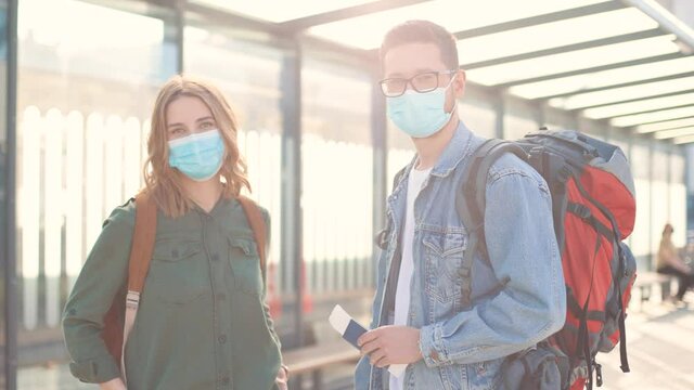 Portrait of Caucasian young cheerful married couple wife and husband in masks standing with backpack and passport traveling during coronavirus looking at camera. Travel safe, travellers, vacation