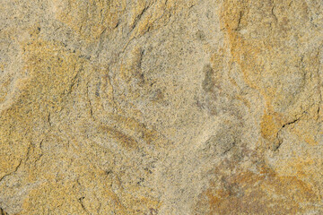 The texture of the uneven surface of the yellow sandstone stone with streaks and gray spots.