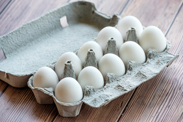 A cardboard egg box with ten white eggs on a wooden table. Eggs in a box
