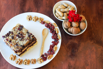Piece of tasty chocolate-nut cake on a white plate. Walnuts and wooden spoon stand nearby