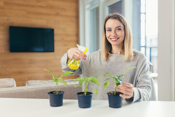 Young beautiful blonde woman, at home takes care of flower pots, pours flowers sitting at the table