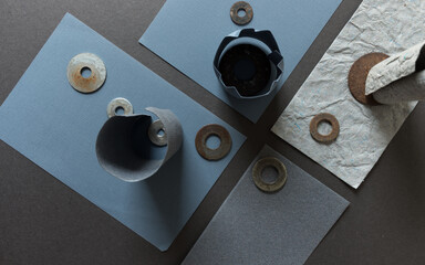 various pieces of rectangular construction paper arranged on grey mat board with rolled pieces and rusty metallic washers - photographed from above in a flat lay style