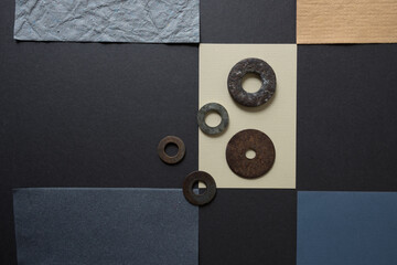 pieces of yellow-ochre and grey paper arranged in a checkered pattern with various metallic washers on a grey board - photographed from above in a flat lay style