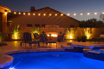 A night shot of a desert landscaped house in Mesa Arizona with an outdoor fireplace, pool and spa.