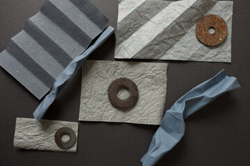 composition in textured, grey papers arranged with rusty metallic washers on a dark grey mat board - photographed from above in a flat lay composition