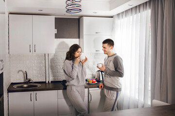 Fototapeta premium Young man and woman are drinking hot coffee or tea with cupcakes and smiling at each other. The family is having breakfast and having a great time. Happy family relationship of heterosexual couple