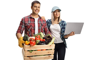 Young male and female farmers with a crate full of vegetables and a laptop computer