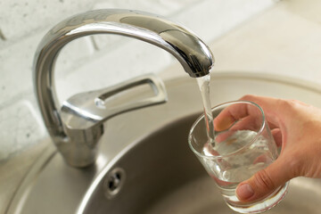 A hand with a glass draws water from the kitchen tap.