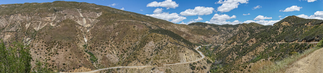 Fototapeta na wymiar Los Padres National Forest, CA, USA - April 8, 2010: Wide panorama view of brown and green forested mountain flanks and tops with road 33 meandering in western part of park.