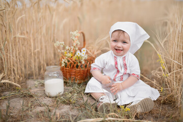 A small child with a glass of cow's milk in a wheat field. World Milk Day. Fresh, healthy milk. Healthy eating. The girl is dressed in national Belarusian clothing with a red ornament.