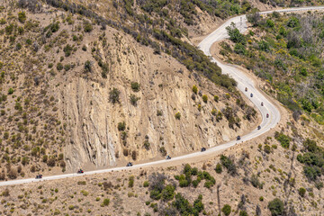 Los Padres National Forest, CA, USA - May 21, 2021: Line of motorcycles ride on road 33 in werstern part of park in front of beige tall cliff on mountains with green sparse vegetation