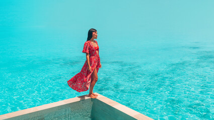 Elegant asian woman relaxing at luxury pool resort overlooking turquoise ocean in red beach coverup...