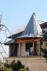 Part of old unusually shaped suburban family house with tower like edge under renovation covered with nylon protection surrounded with trees on blue sky background