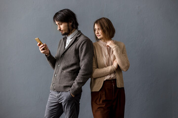 Man looks at the phone and the woman peeps from back. Gray background.