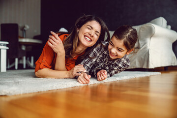 happy mother and daughter lying down on the floor at home and laughing. Love is only important thing for happy family.
