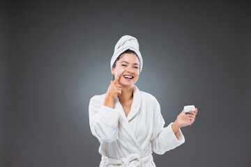 Beauty hydrating moisturizer and skincare routine. Woman in a bathrobe and a towel holds the cream...
