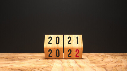 cube turns from 2021 to 2022 on wooden base and chalkboard background - obrazy, fototapety, plakaty