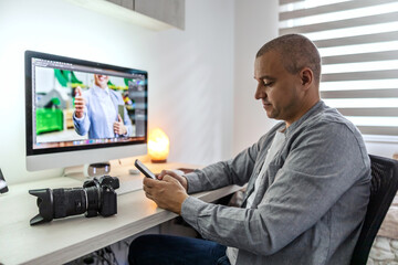 Fototapeta na wymiar Surfing the internet on the phone during breaks A man in gray clothes is waiting for the approval of photos from a client in the home office in the apartment Preparing to take a photo with the camera