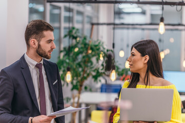 Manager explaining to his employee how to finish her tasks. Colleagues discussing a project while standing in an office.