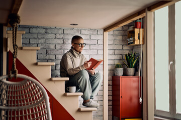 Senior woman with short hair sitting on stairs at home and reading an interesting book.