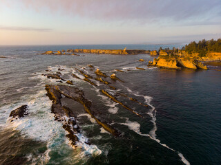 Aerial panorama of the rocks at the entry to the Sunset Bay, Oregon Coast at sunset. Light house of Chiefs island in the background.