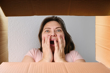 woman opened a cardboard box with an ordered product and emotionally reacts to its contents, the concept of a postal item, a package, buying goods online, surprises