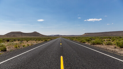 Straight asphalt road with dashed yellow strip line running between hills into horizon. A road in a high desert of South Oregon