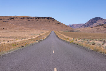 Old straight asphalt road with yellow dashed line leading into the horizon in the middle of nowhere, south Oregon.