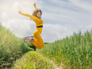 a blonde runner girl in yellow running tights jumps in the middle of a crop field. sunny day. the girl is happy and enjoys doing sport. concept of happiness and freedom in the open air.