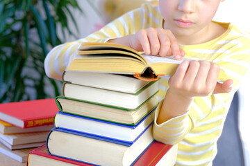 boy, schoolboy in yellow t-shirt sitting at home, in front of him large pile of paper books, reading, concept of tiredness from school assignments, lot of home lessons, education concept, fiction