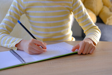 child, schoolboy in yellow t-shirt, writes letters in notebook with an pencil, bright backlight,...
