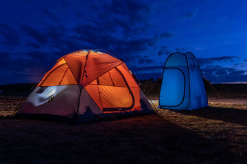 Orange camping tent and blue shower tent on a camping ground under evening sky.