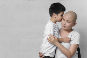 Young adult female cancer patient spending time with little son on gray background. Cancer and family support concept.
