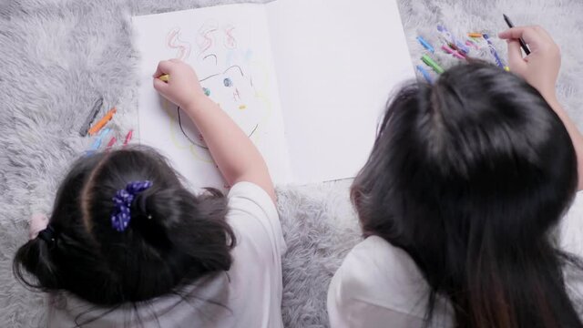 Top and back view of mom and kid lying on the floor doing painting by coloured pencils and talking together in living room with lots of happiness