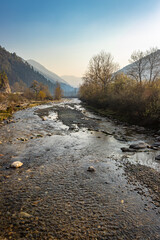 river flowing through misty mountain valley covered with dense forests at dawn from flat angle