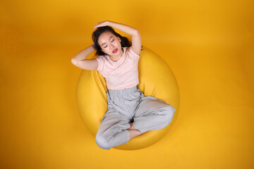 Beautiful young south east Asian woman sits on a yellow beanbag seat orange yellow color background pose fashion style elegant beauty mood expression rest relax think emotion top view